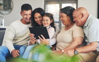 Three generations of a family smiling together on a sofa while looking at a tablet, representing estate planning, family legacy, and future financial security for Utah families.